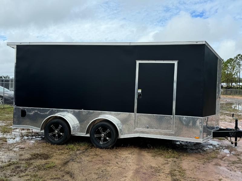 A black trailer with a silver door, parked on muddy ground next to a fence.