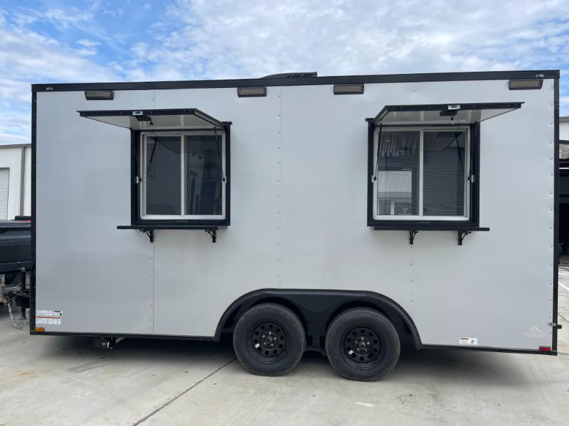 The image shows a large, white, enclosed trailer with two windows on the side, parked outdoors under clear skies.