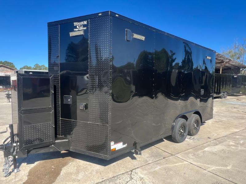 The image shows a black enclosed trailer parked on a concrete surface with a clear sky in the background.