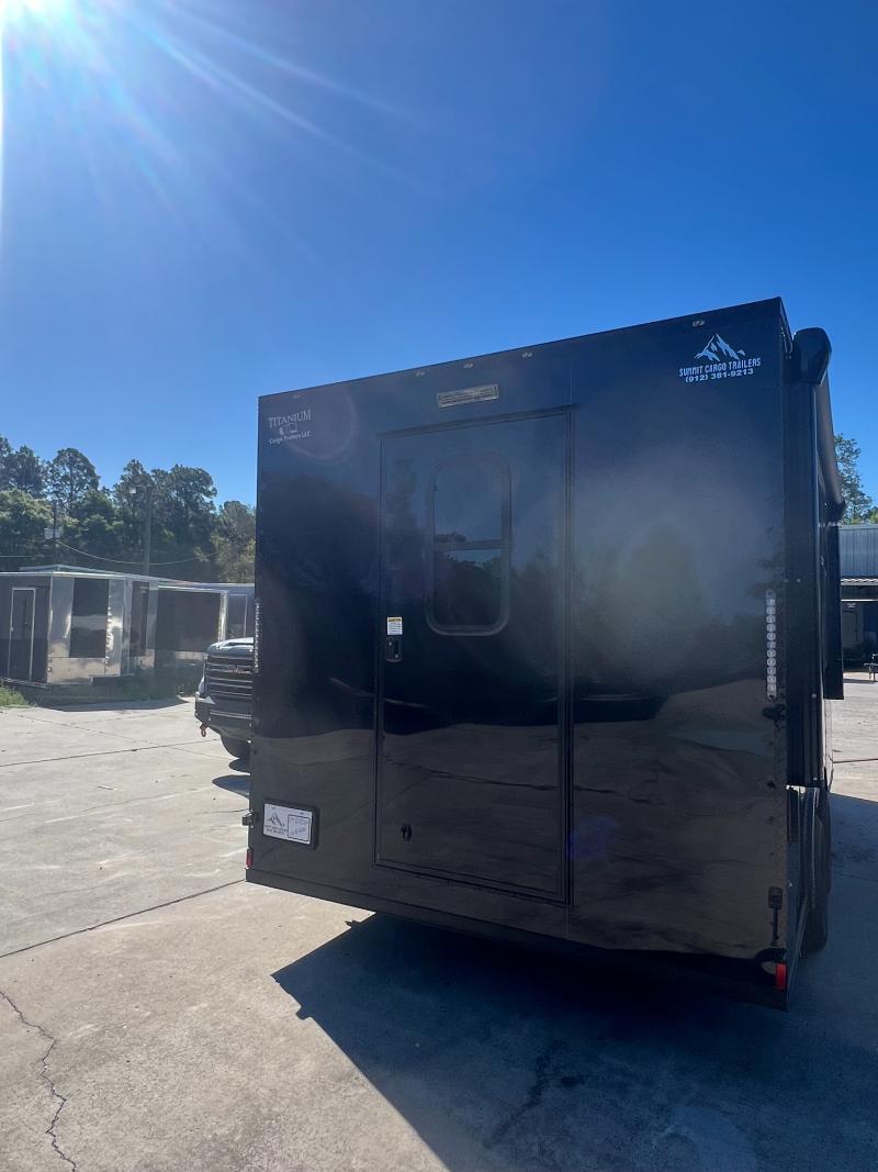 The image shows a black enclosed trailer parked outdoors during daytime under clear blue skies.
