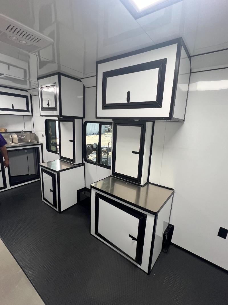 The image shows a spacious kitchenette area with white cabinets, black countertops, and stainless steel appliances, including a refrigerator, oven, and sink.
