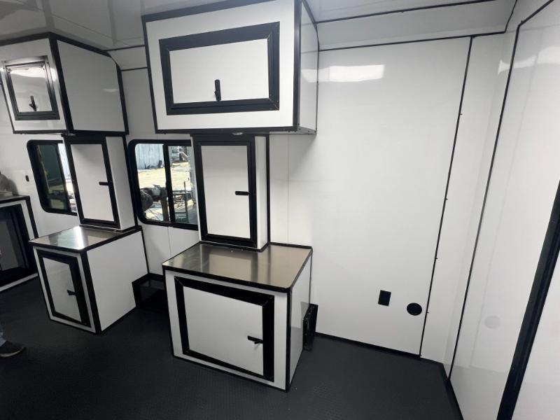 The image depicts a modern kitchen interior with sleek cabinetry in black and white, featuring multiple wall-mounted cabinets, a table with a stainless steel surface, and a large refrigerator.