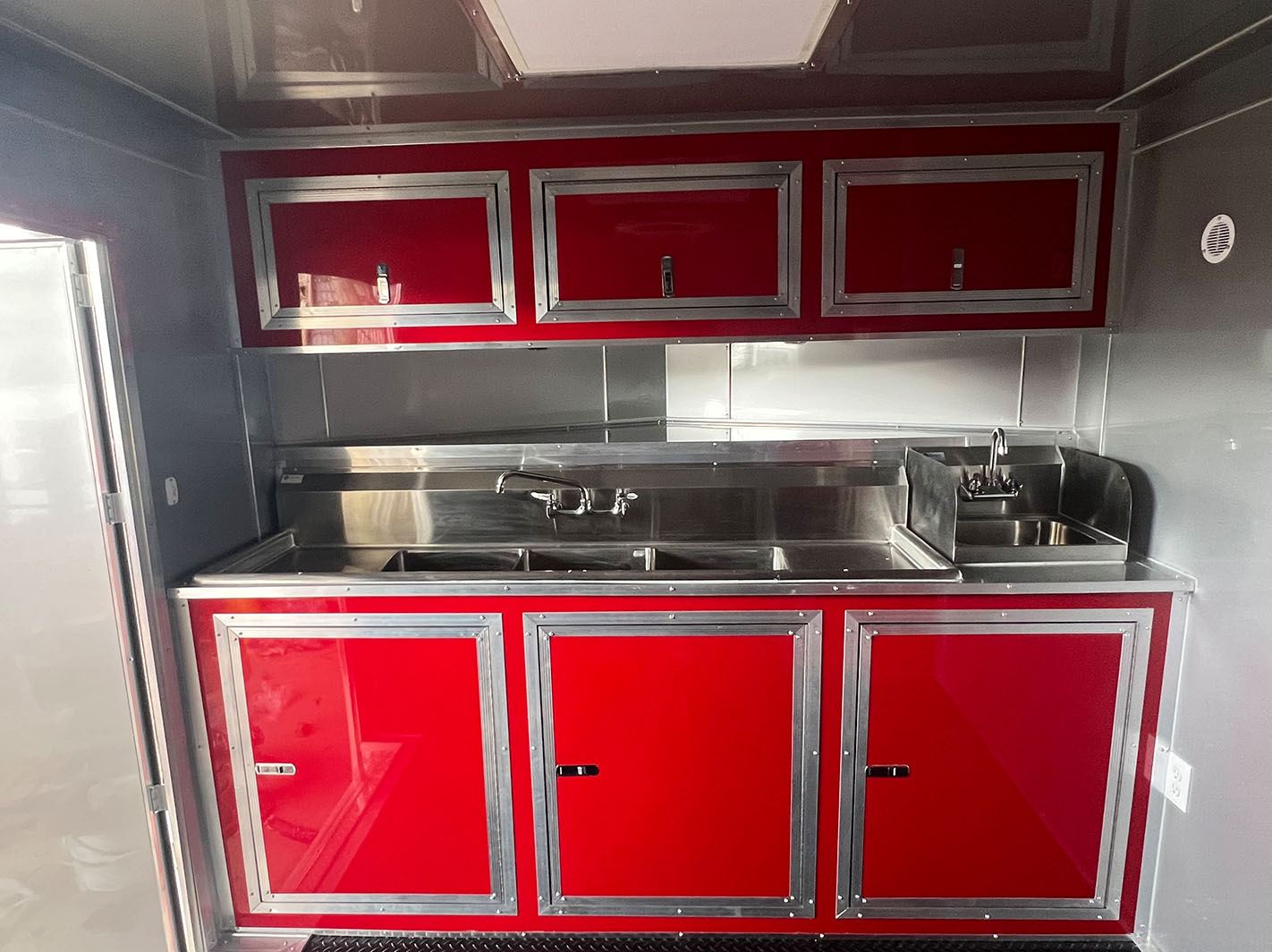 The image shows a red kitchen cabinet with white handles inside a vehicle, likely a camper or motorhome.