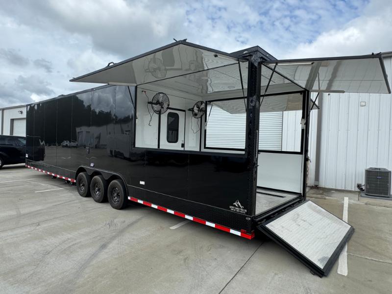 The image shows a large black enclosed trailer parked on an asphalt surface with a clear sky above.