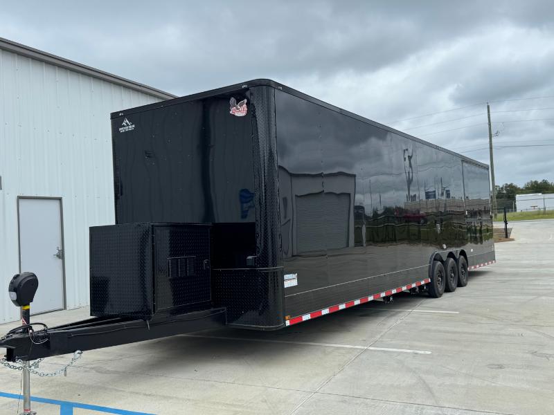 The image shows a large black enclosed trailer parked on an asphalt surface, with a clear sky visible in the background.