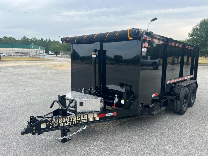 The image shows a large black utility trailer with a flatbed, parked on an asphalt surface, with a truck cab visible in the background.