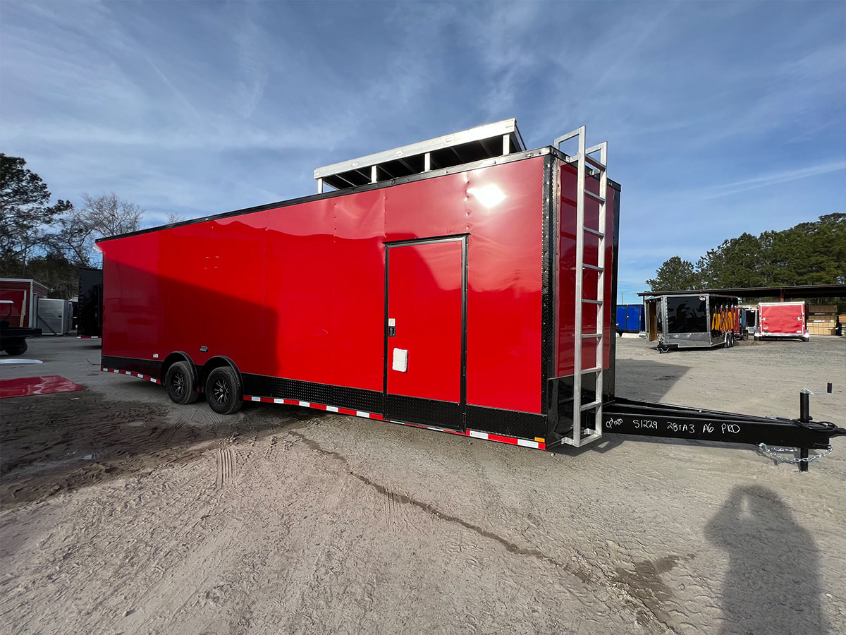 A large red enclosed trailer parked on dirt ground with a clear sky background.