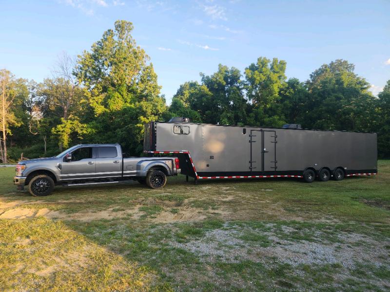 A large black mobile trailer parked on grass next to a pickup truck.