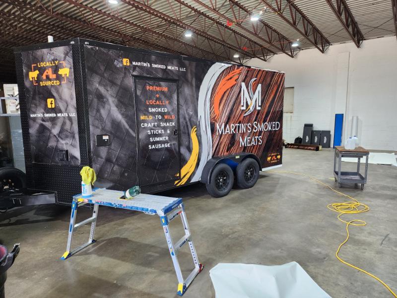 The image shows a large food truck parked inside a building with its side door open, revealing branding and interior equipment.