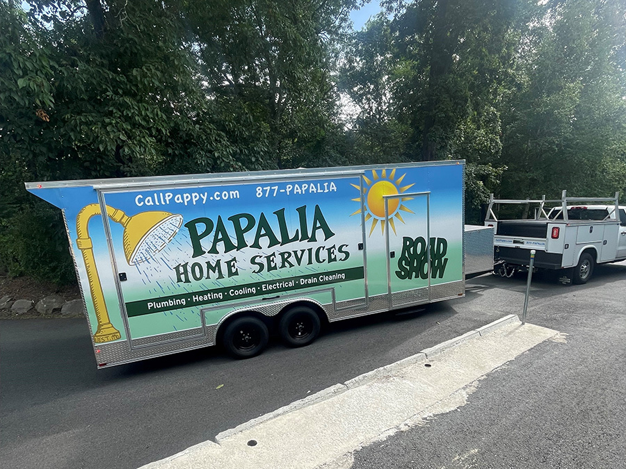 The image shows a large truck parked on the side of a road with a sign advertising Papalia home services, including a logo with a sun and a water spout, and a phone number displayed.