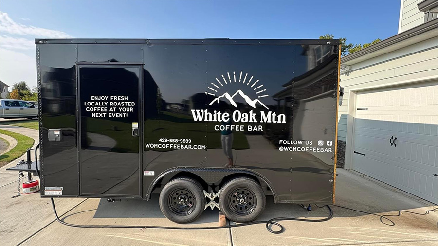 The image displays a large black truck parked next to a building with a sign that reads White Oak Mtn.