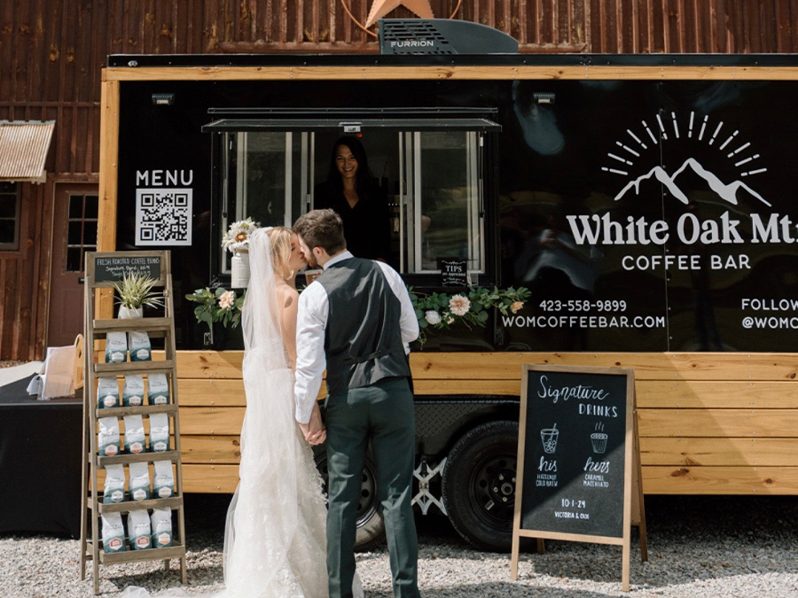 A couple standing in front of a food truck with White Oak Mtn Coffee Bar written on the side, sharing a kiss.