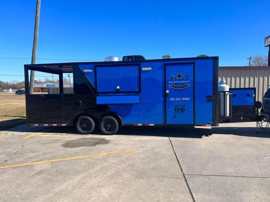 The image displays a blue food truck parked in a lot with a clear sky above.
