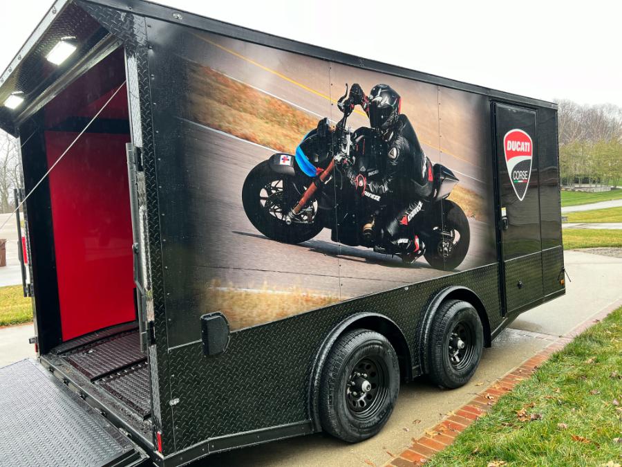 An image of a large black trailer with an advertisement featuring a motorcycle rider on it parked outdoors.