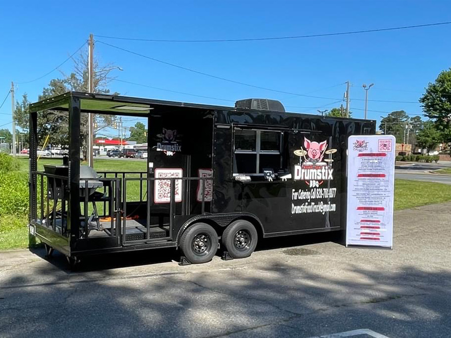 The image shows a black food truck parked outdoors during the daytime.