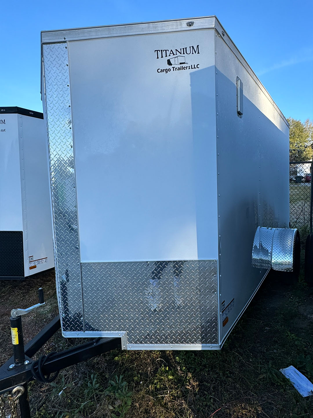 The image shows a large white trailer with a silver roof parked on a grassy area, possibly at an event or a storage lot.