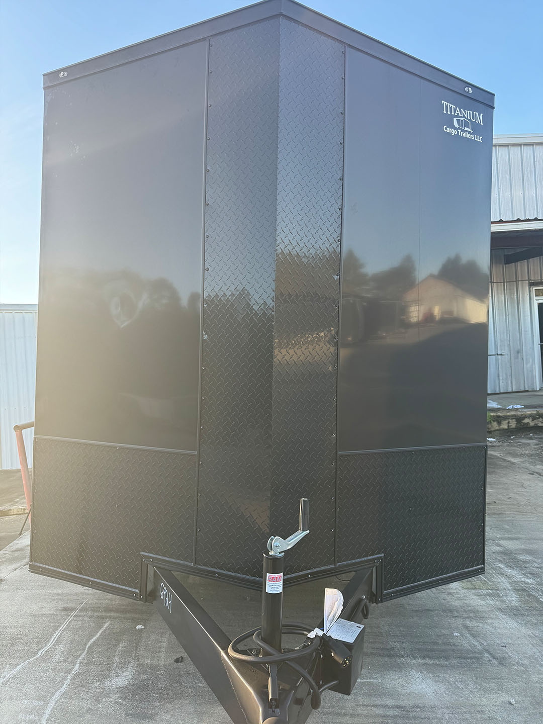 The image shows a large black shipping container with a metal pattern on its side, placed outdoors during daylight hours.