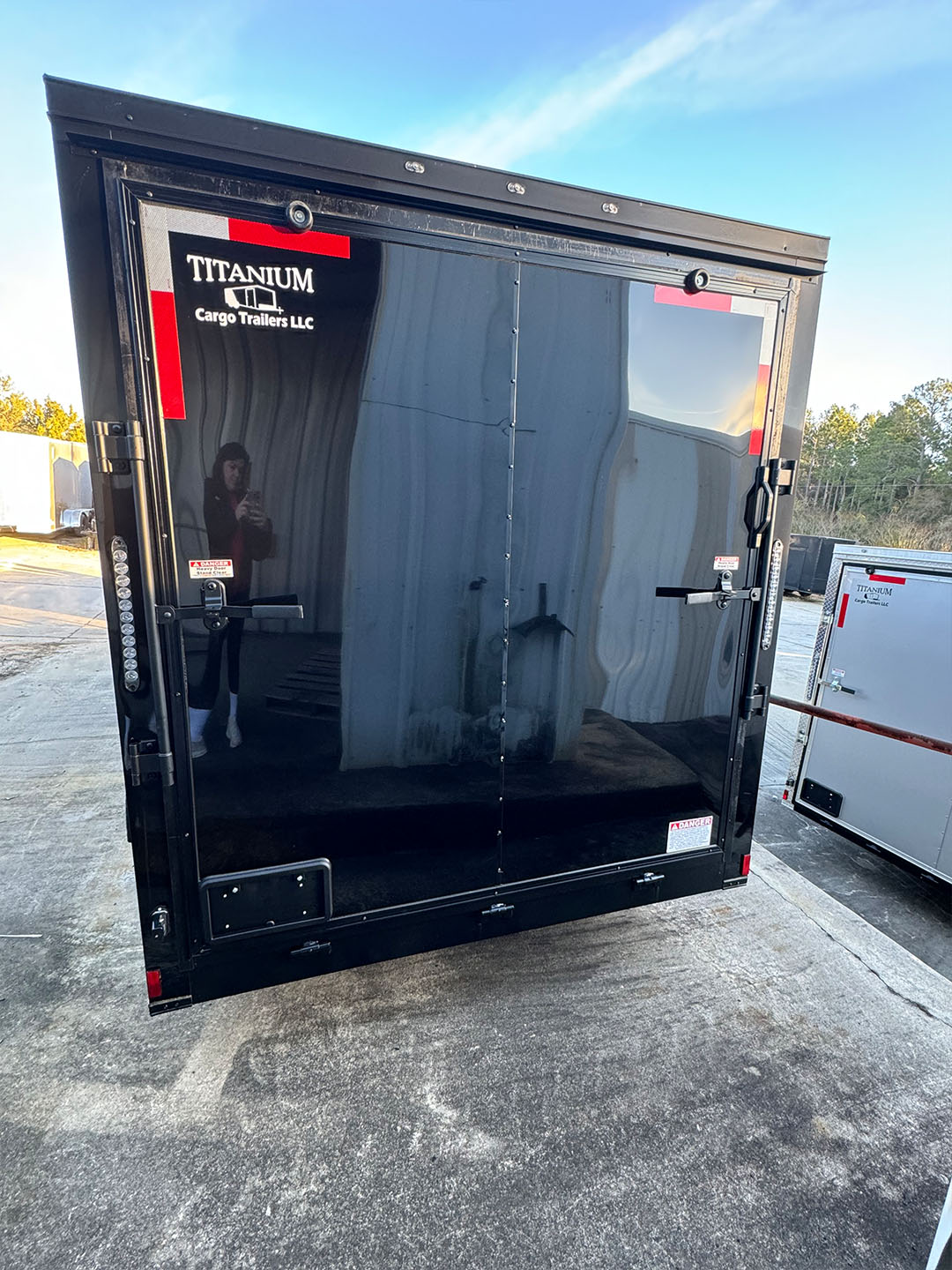 The image shows a black delivery truck parked outdoors with its door open, against a clear sky.