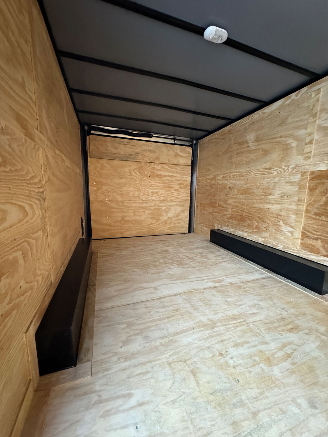 This is an interior view of an empty truck with plywood walls, featuring a black floor and a white ceiling, ready for loading.
