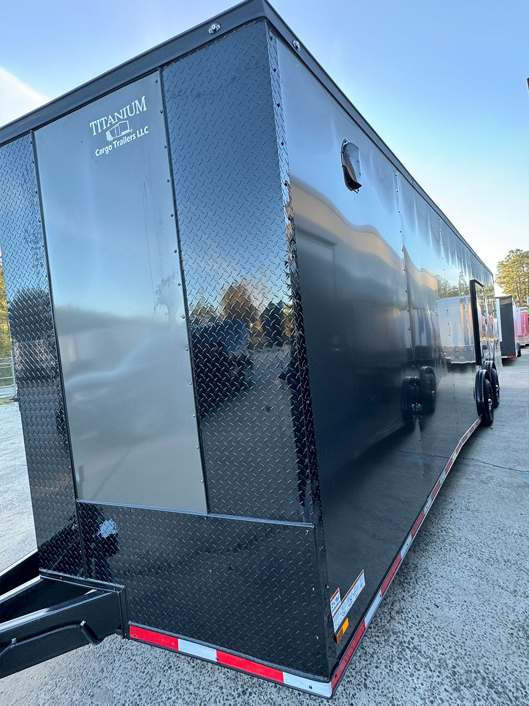 The image depicts a large black trailer with an open door parked on a paved surface.