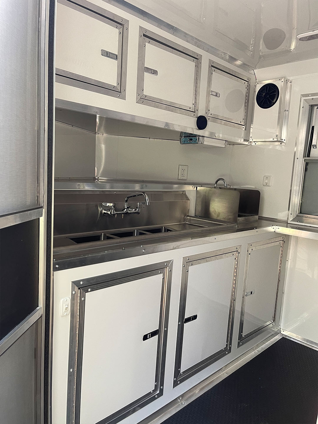 The image shows a well-equipped kitchen inside a recreational vehicle  RV , featuring stainless steel appliances, including a sink, stove, and refrigerator, with white cabinetry and a metallic finish.