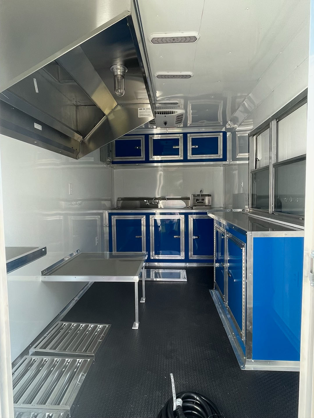 The image shows an interior view of a commercial kitchen with stainless steel appliances, blue cabinetry, and a metal countertop.