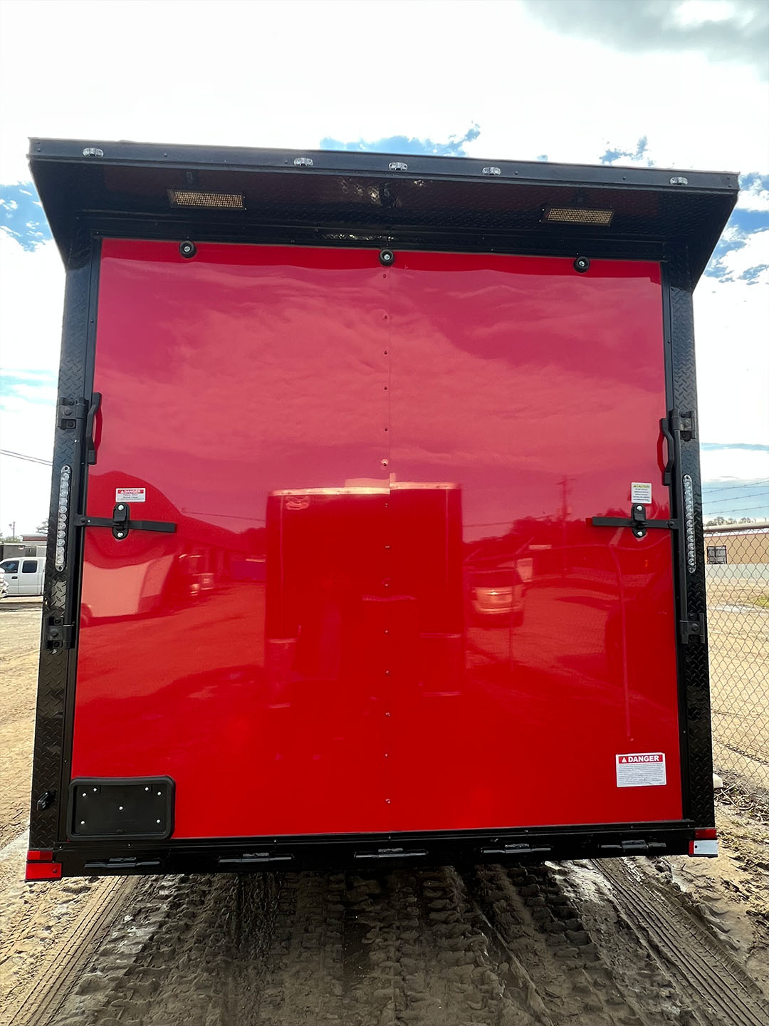 An image depicts a red commercial truck parked on a dirt surface with a clear sky above.