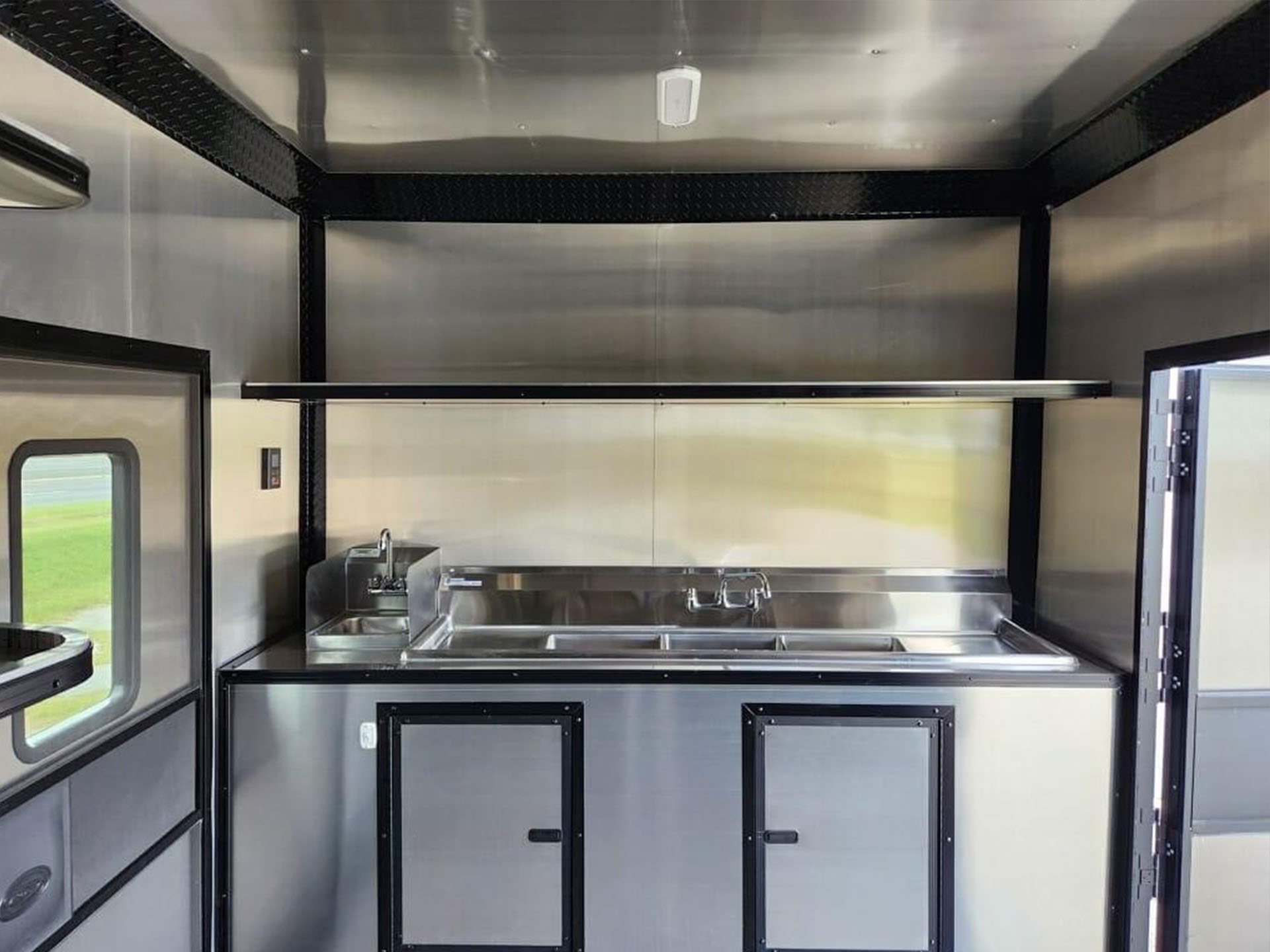 The image shows a large stainless steel commercial kitchen with appliances, countertops, and a sink inside a vehicle.