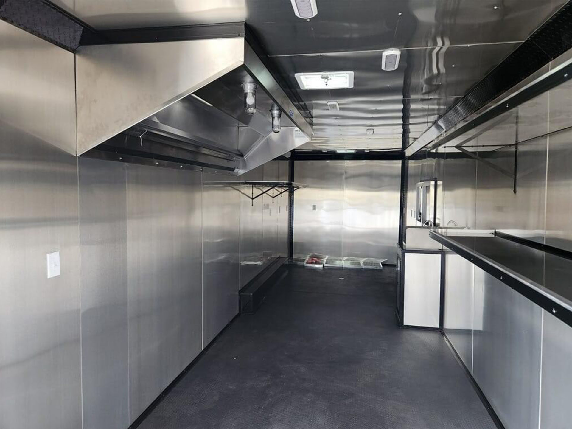 The image shows a stainless steel commercial kitchen interior with shiny surfaces and various appliances, including a large refrigerator and an oven.