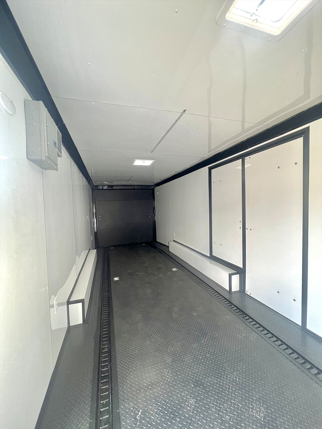 The image shows an empty cargo space inside a truck trailer with white walls and a dark floor, viewed from the rear door area.