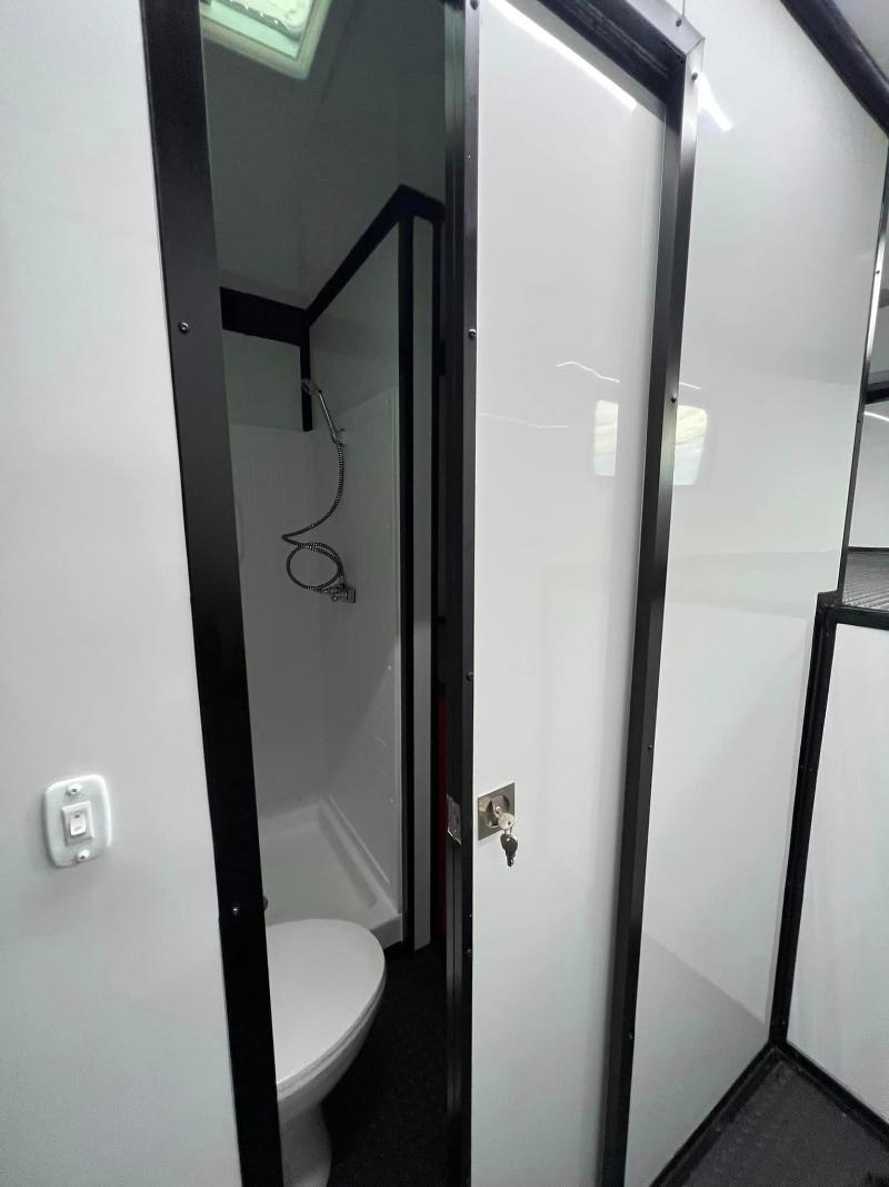The image shows a modern bathroom interior with a white toilet, black flooring, and a shower area enclosed by transparent glass panels.