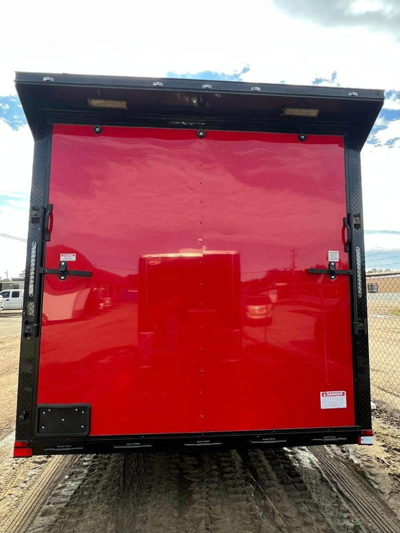 The image shows a large red trailer truck with its doors closed parked on a gravel surface under a clear sky.
