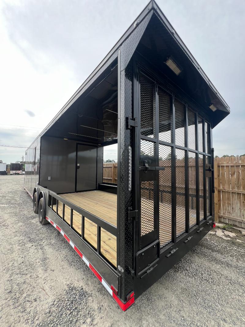 This image features a black enclosed trailer with a side door and a rear window, parked on a gravel surface.