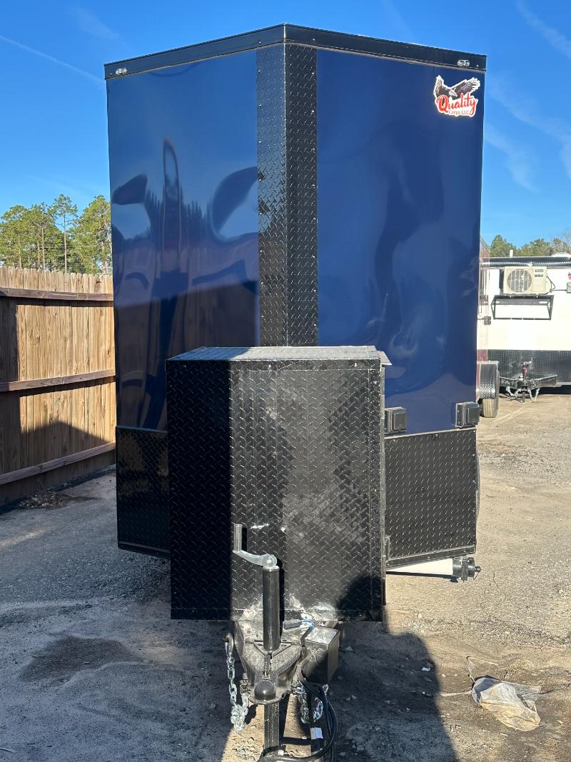 The image shows a blue trailer with an enclosed back area parked on a paved surface, possibly at a construction site or similar location, with a clear sky above.