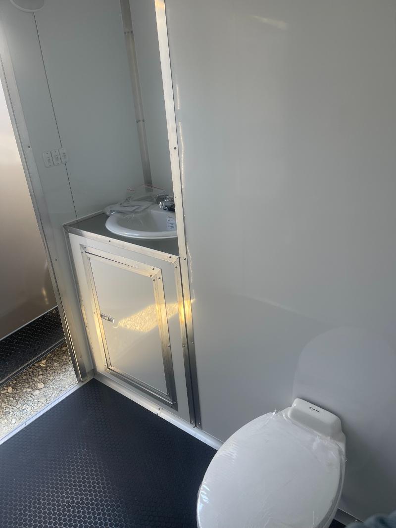 The image shows a small bathroom inside a vehicle, with a toilet on the right and a sink with a mirror above it on the left wall.