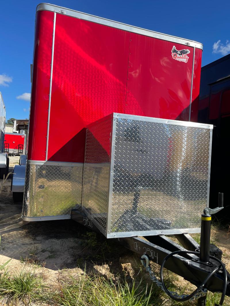 The image shows a large red horse trailer parked outdoors on a dirt surface with a clear sky above.