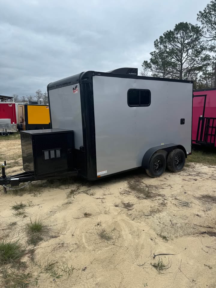 A gray horse trailer parked on sandy ground.