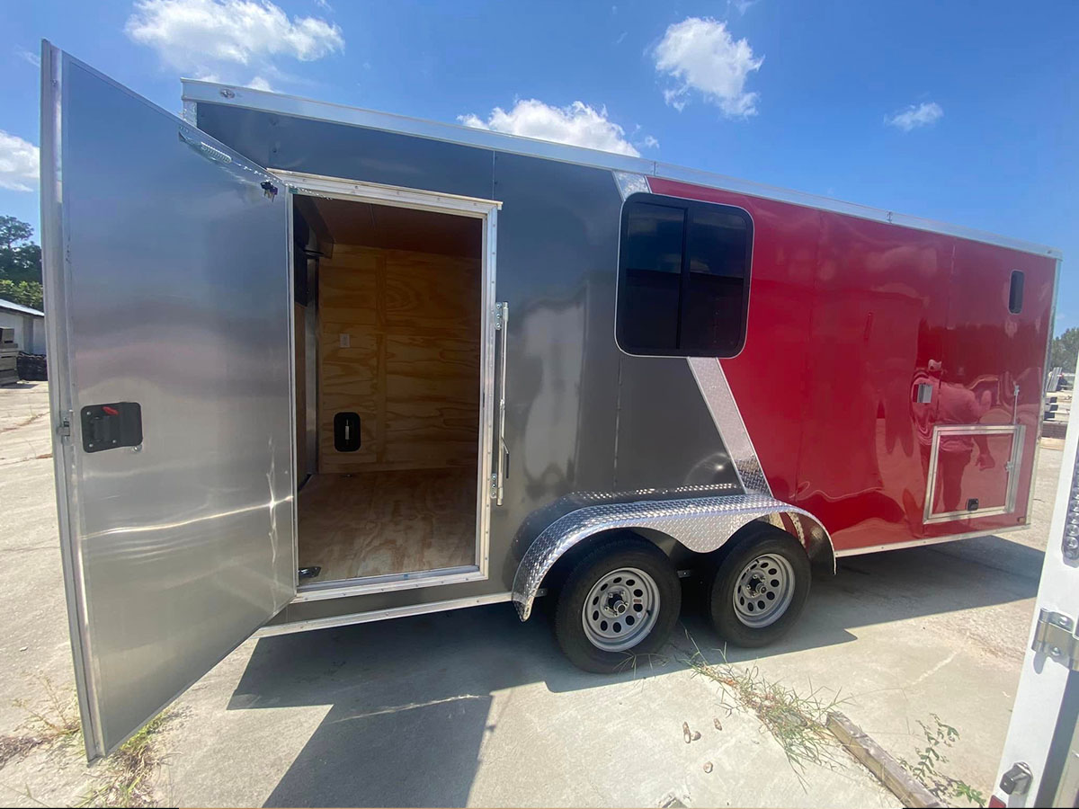 The image displays a red and silver trailor parked on an open lot with its door open, providing a view into the interior.