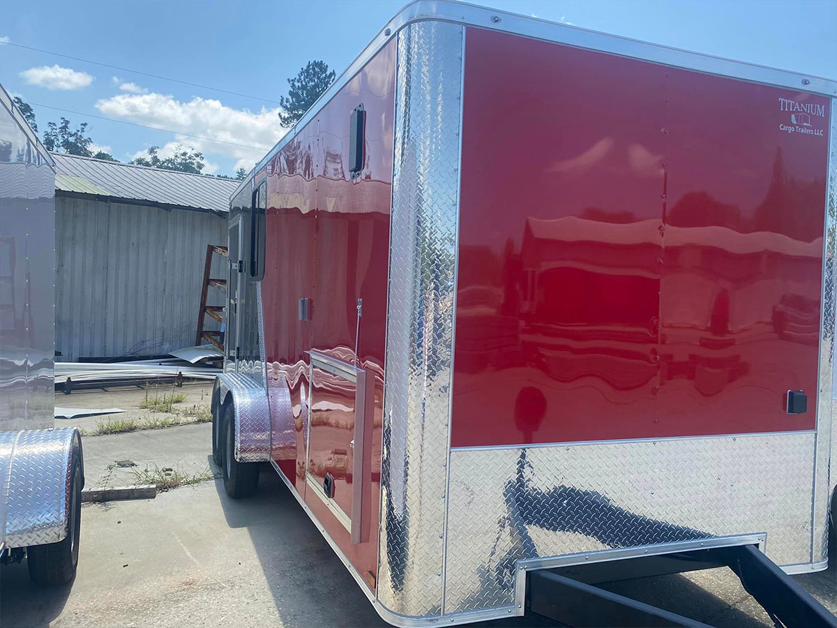 The image displays a large red enclosed trailer parked on a surface with a clear sky above.