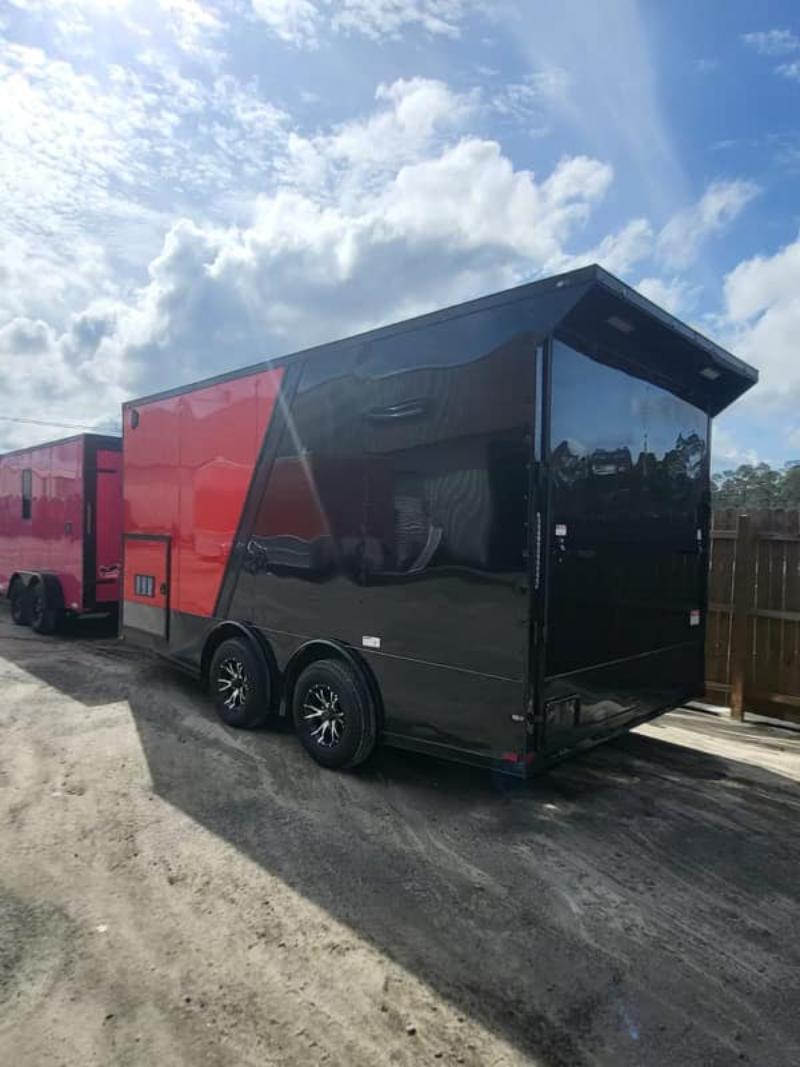 A large black trailer parked next to a red truck.