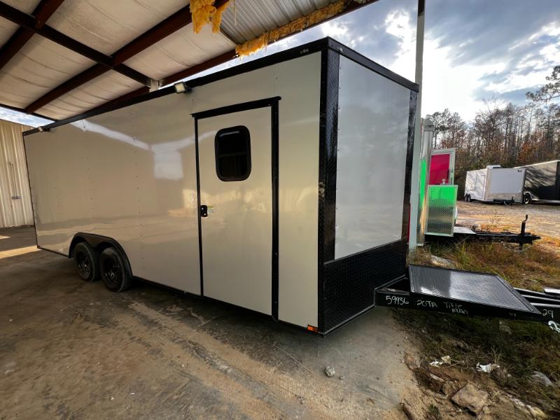 The image depicts a black and white horse trailer parked on a gravel surface under an open structure with metal walls.