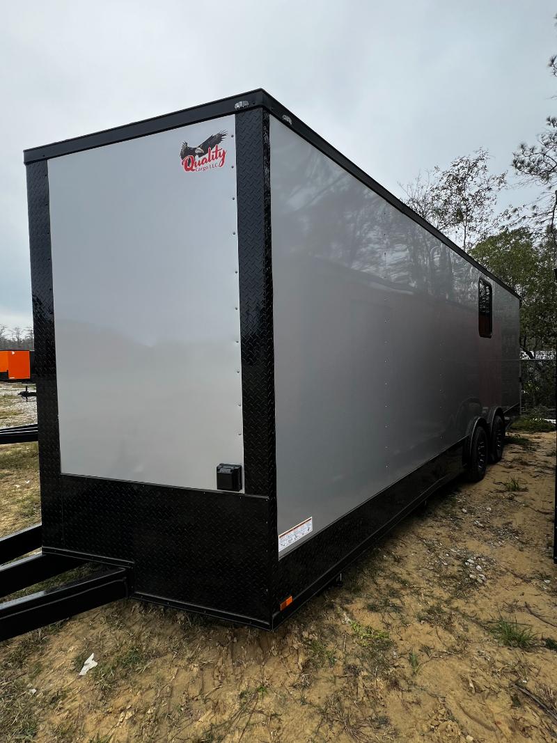 This is an image of a black enclosed trailer parked on a gravel surface with a clear sky in the background.