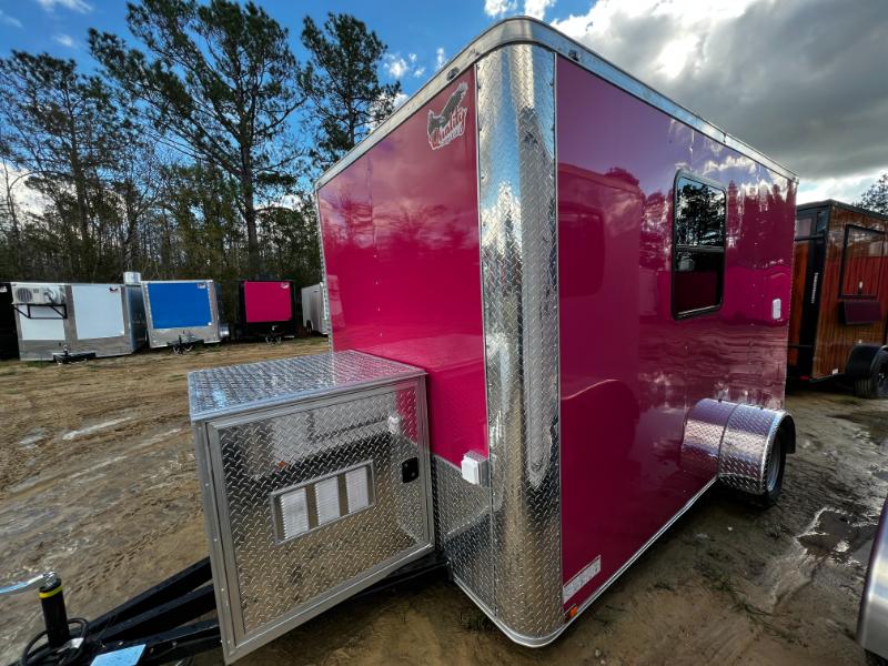 A large pink horse trailer parked on a dirt lot with a clear blue sky overhead.