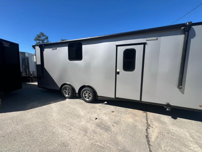 The image shows a large silver horse trailer parked on an asphalt surface with a clear sky above.