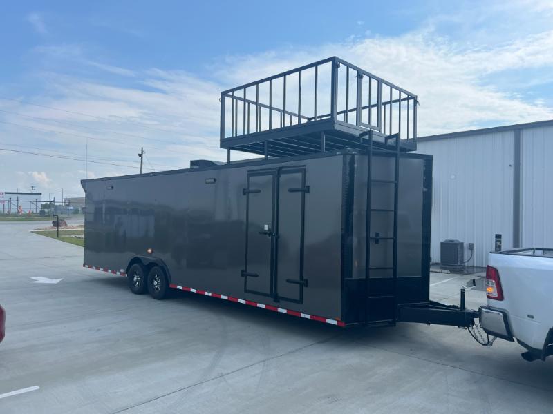 This is an image of a black trailer with a large metal structure on top, parked next to a white truck.