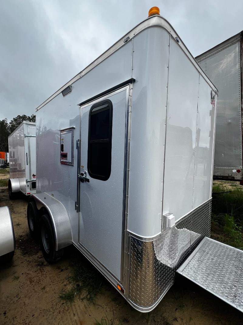 The image shows a large white horse trailer parked on a grassy area with a clear sky above.