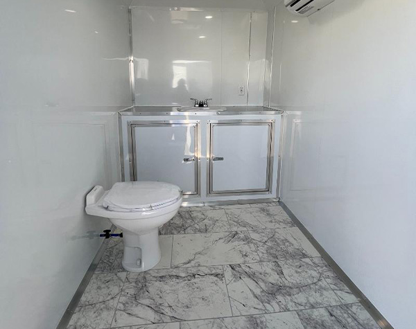 The image shows a small room with a white toilet, a stainless steel sink cabinet, and a marble floor. The walls are covered with white tiles, and there's a window on one side.