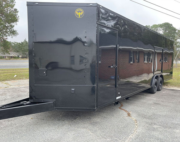 The image shows a black enclosed trailer parked on an asphalt surface.