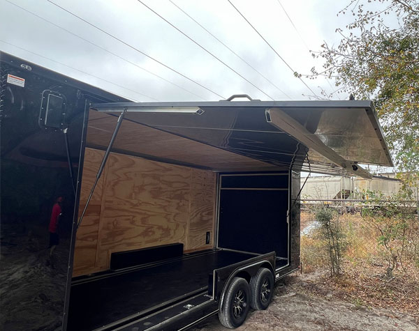 The image shows a black enclosed trailer parked outdoors during daylight hours.