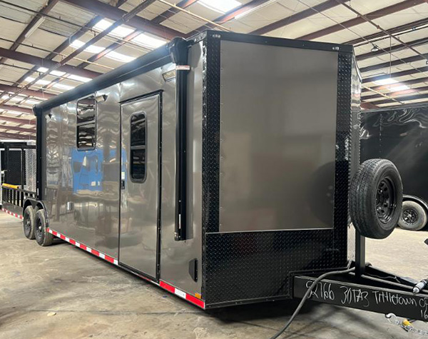 This is an image of a black enclosed trailer parked inside a building with a metal floor and industrial walls.
